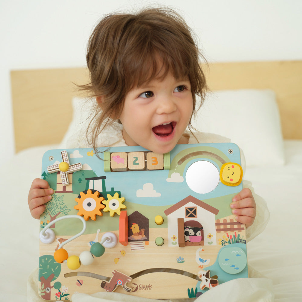 Baby holding the Classic World Farm Busy Board.
