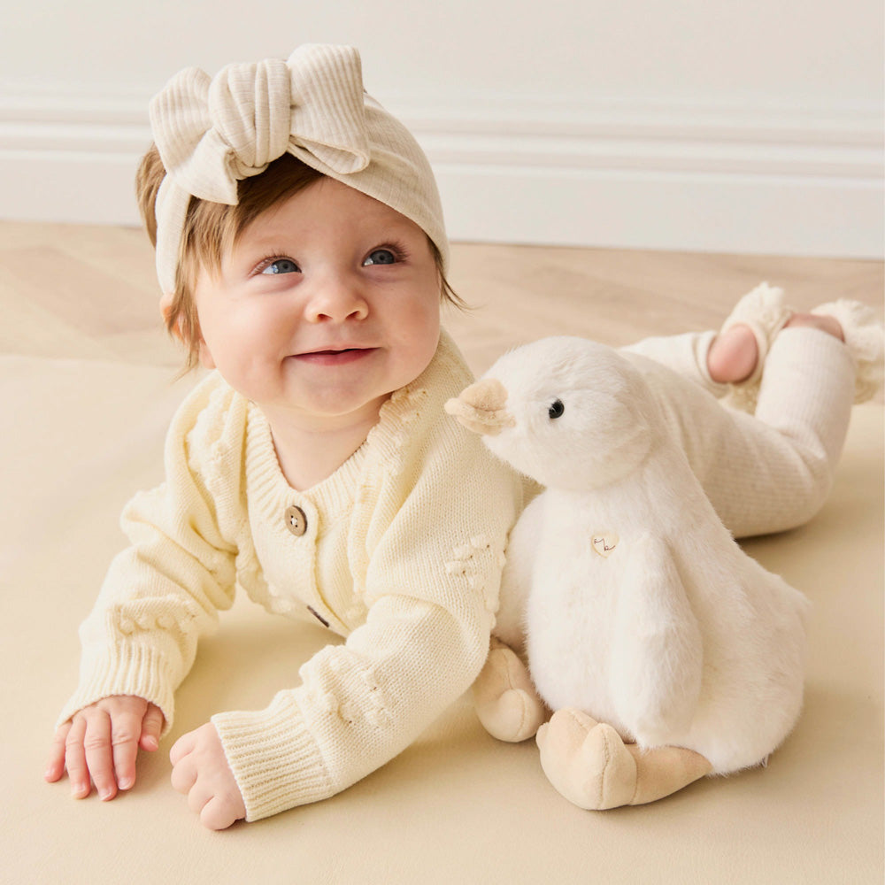 Baby laying on floor with the Snuggle Bunnies Duck Plush soft toy